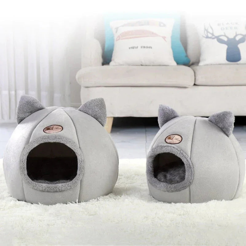 Two gray pet houses shaped like cats on a white carpet 